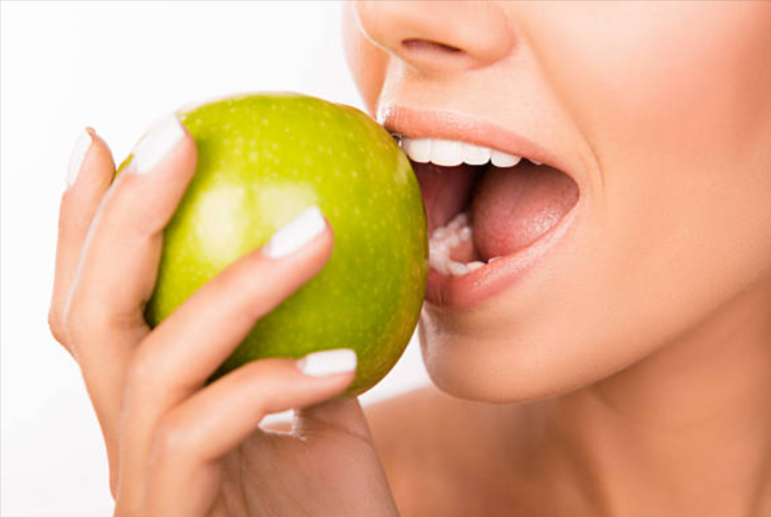 Close-up of woman biting into a green apple with healthy white teeth, symbolizing gum health and prevention of gum disease